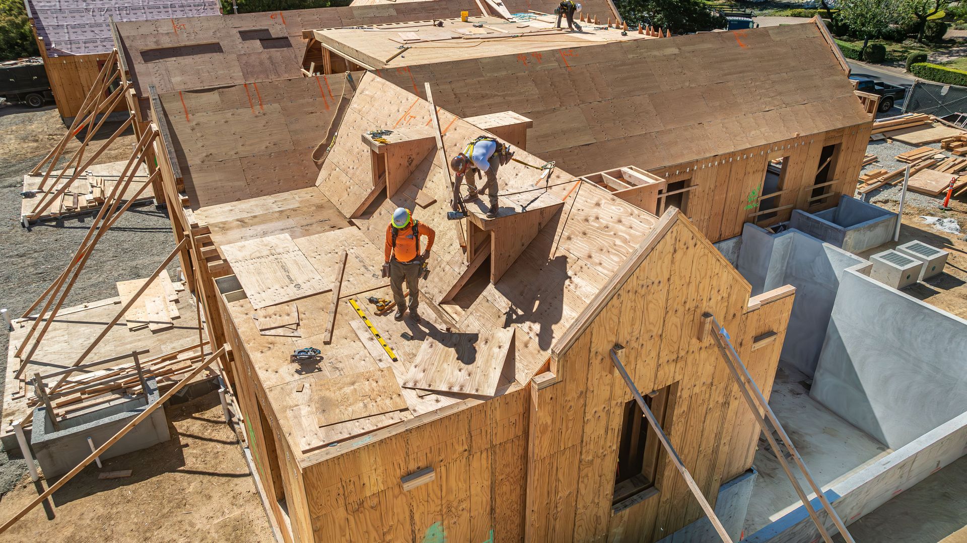 Roofers working on a plywood house roof at a construction site