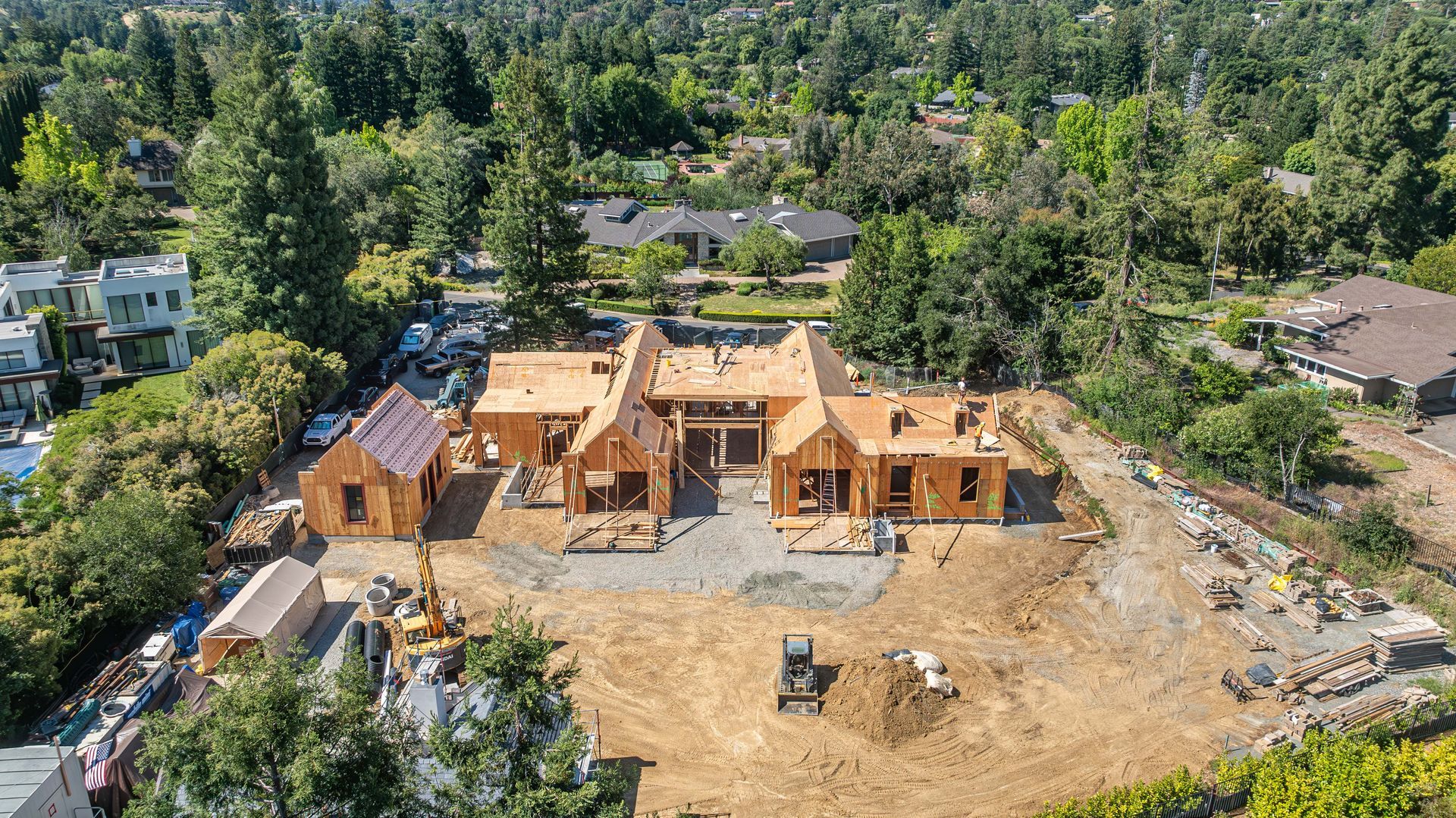 Aerial view of a large wooden house under construction surrounded by trees and dirt lot
