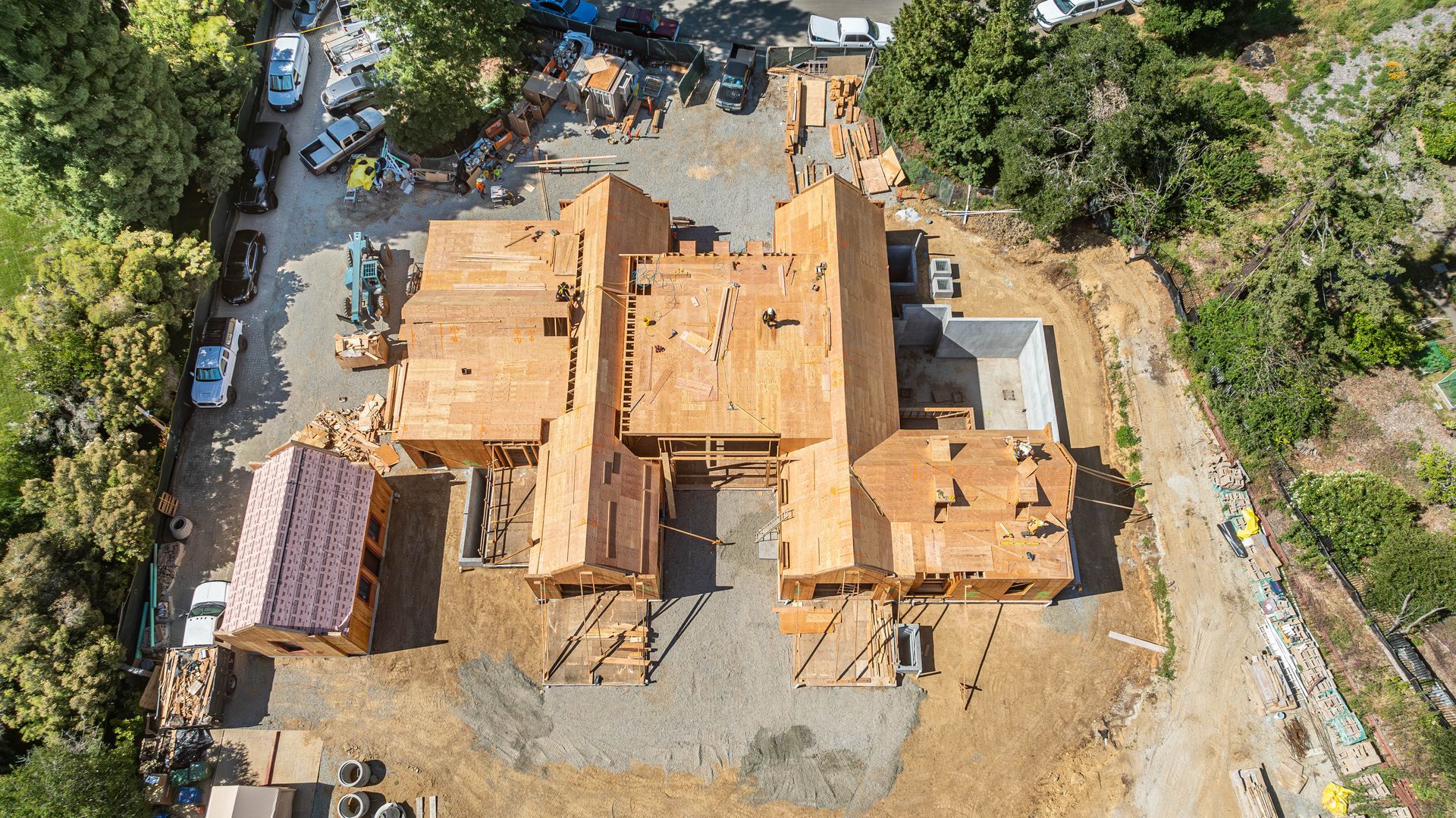 Aerial view of a large house under construction with exposed wood framing and surrounding trees.