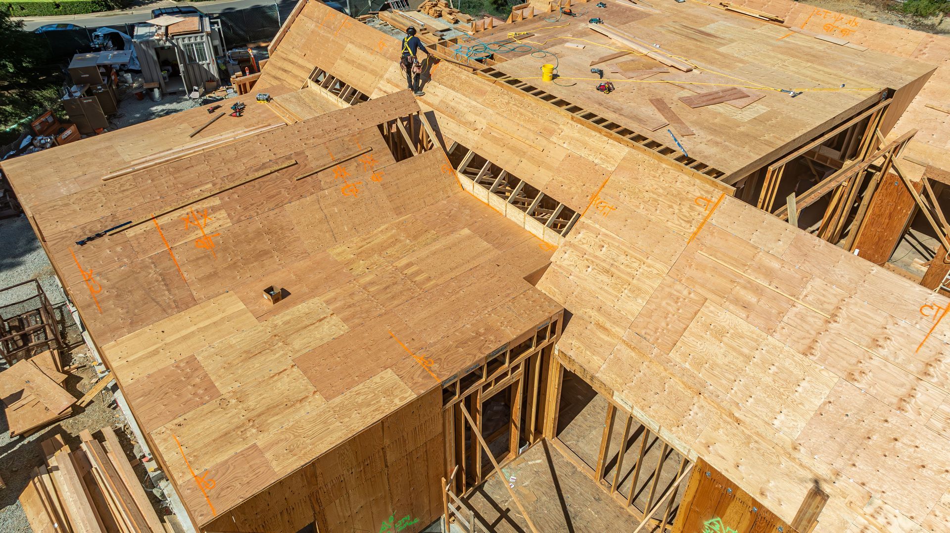 Aerial view of a house under construction with exposed wooden framing and plywood roofing panels