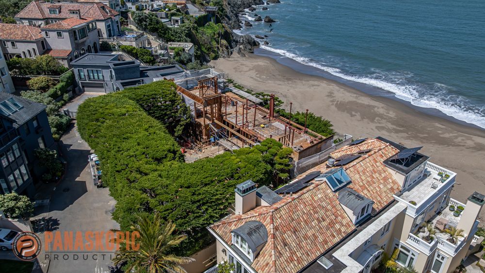 Aerial view of seaside buildings, a green courtyard, and a wooden structure beside a sandy beach.