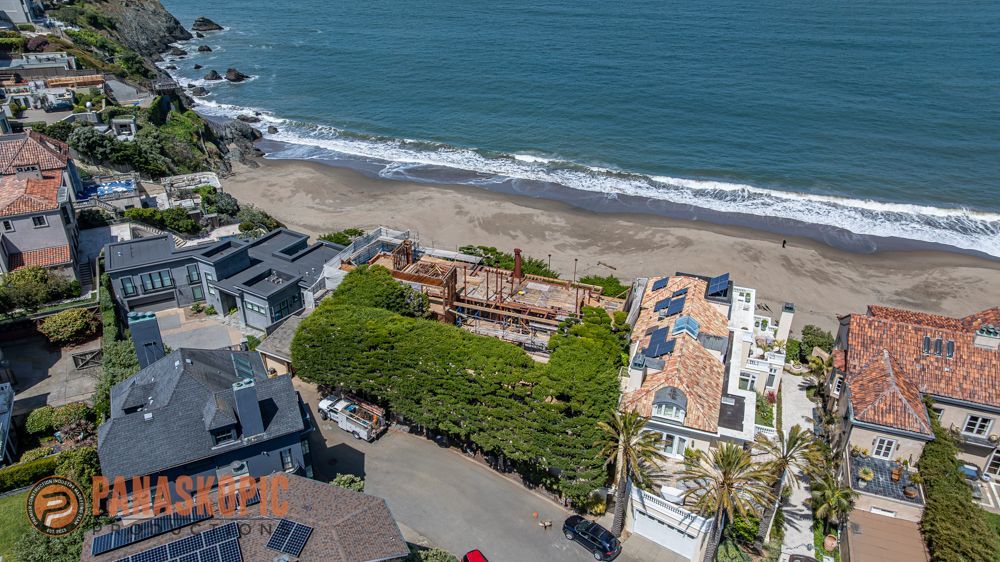 Aerial view of beachfront homes beside a sandy shore and blue ocean, with waves along the coast.