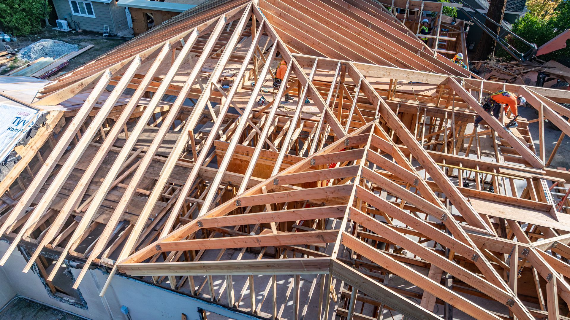 Wooden roof framing under construction on a house, with exposed rafters and trusses.