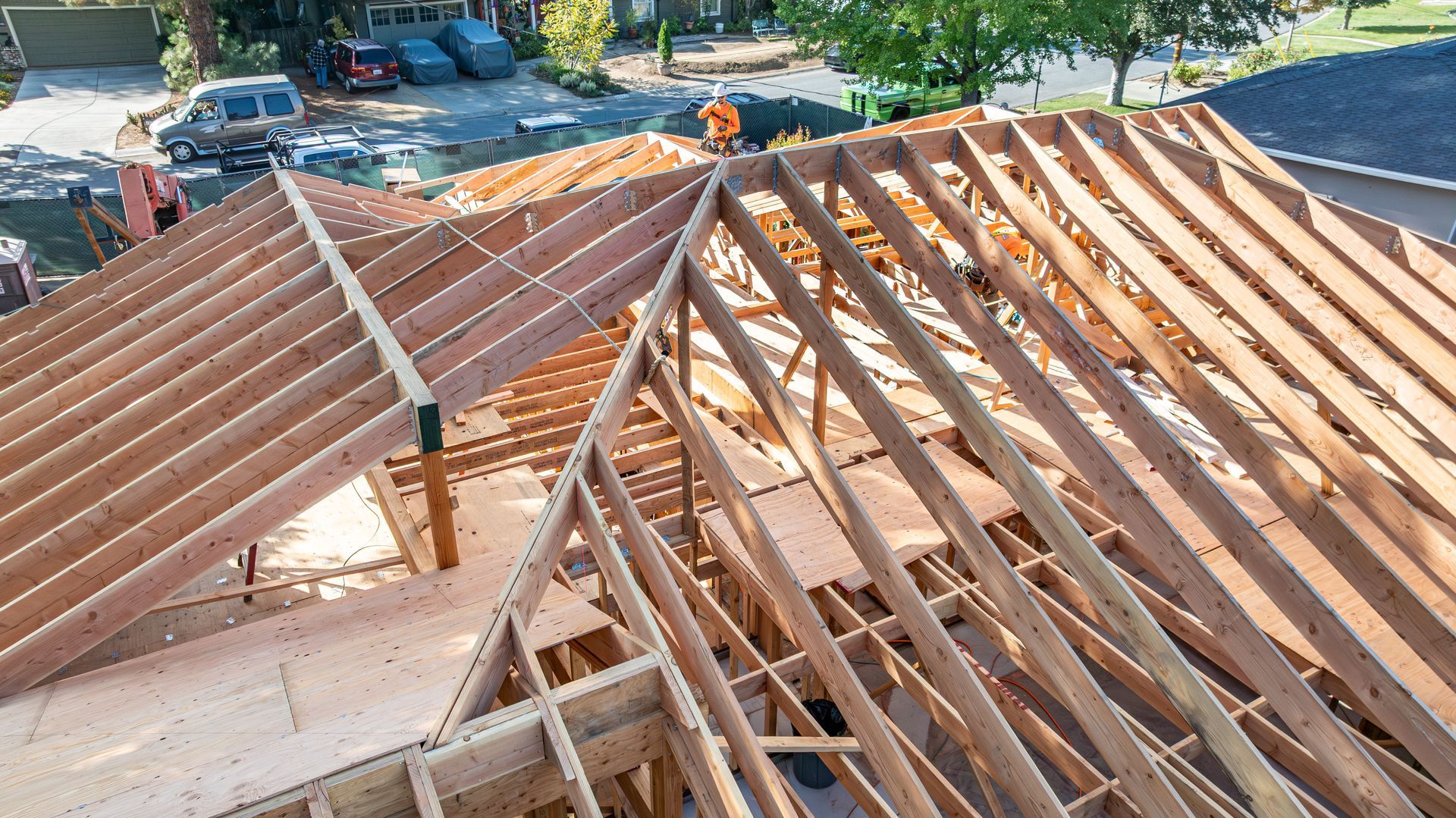 Wooden roof trusses under construction on a house, with exposed framing and parked cars in the background.