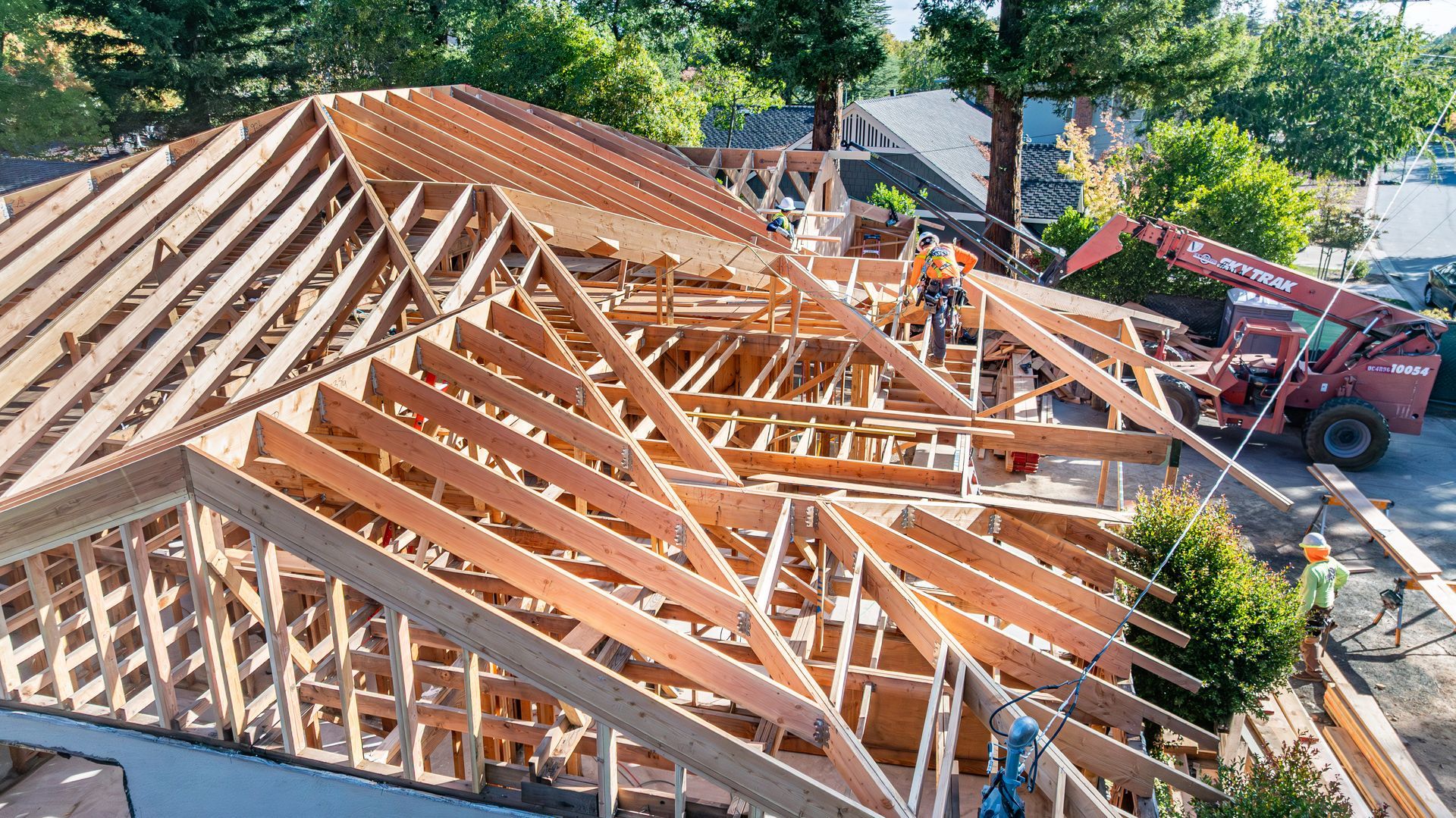 Partially built wooden roof frame on a house with construction equipment nearby
