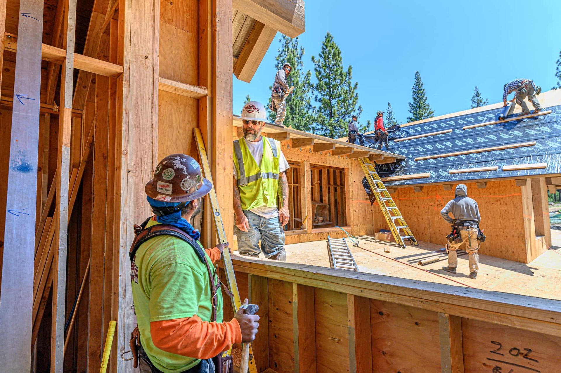 Construction workers framing a wooden house on a sunny site with blue sky.