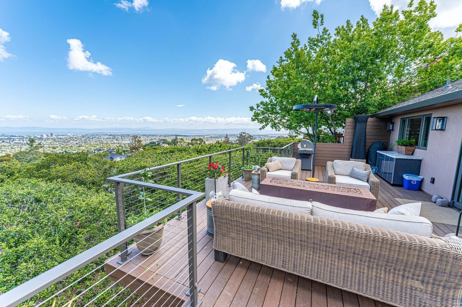 Outdoor terrace with wicker seating, glass railing, and city view under a bright blue sky