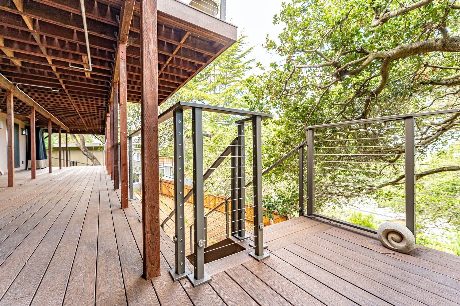Wooden deck with railing and stairs overlooking a leafy forest canopy