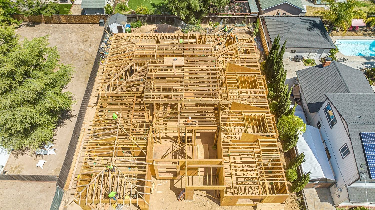 Aerial view of a house under construction with exposed wooden framing and surrounding homes.