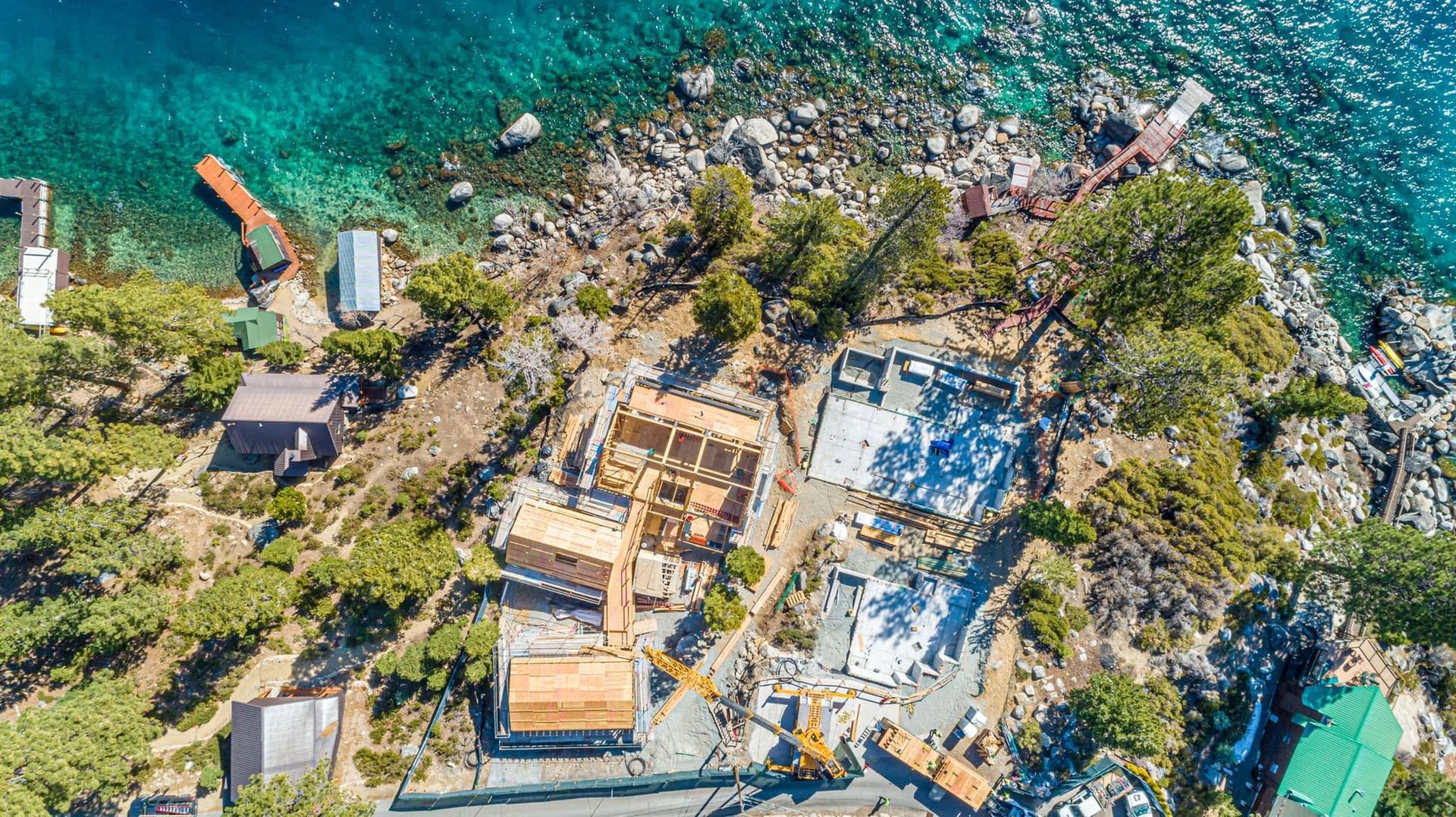 Aerial view of a rocky shoreline with turquoise water, small buildings, and construction debris.