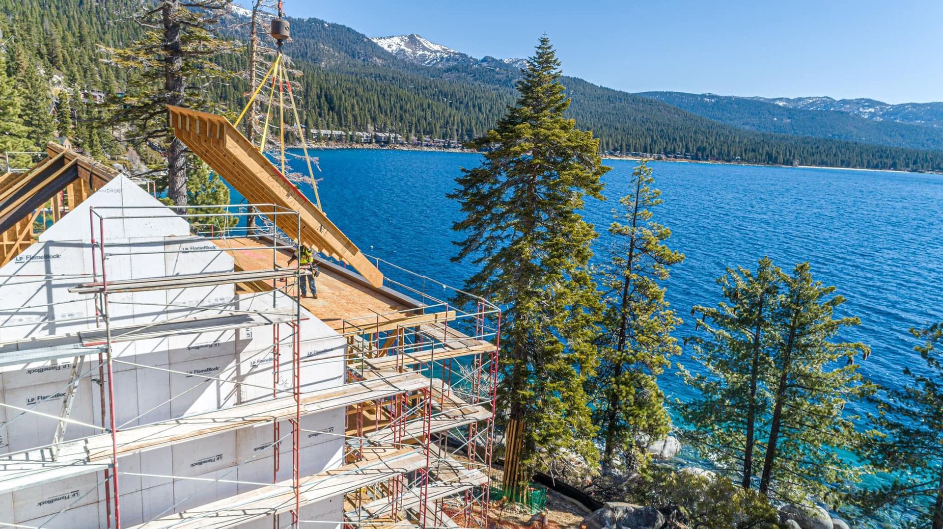House under construction beside a blue lake with mountains in the background