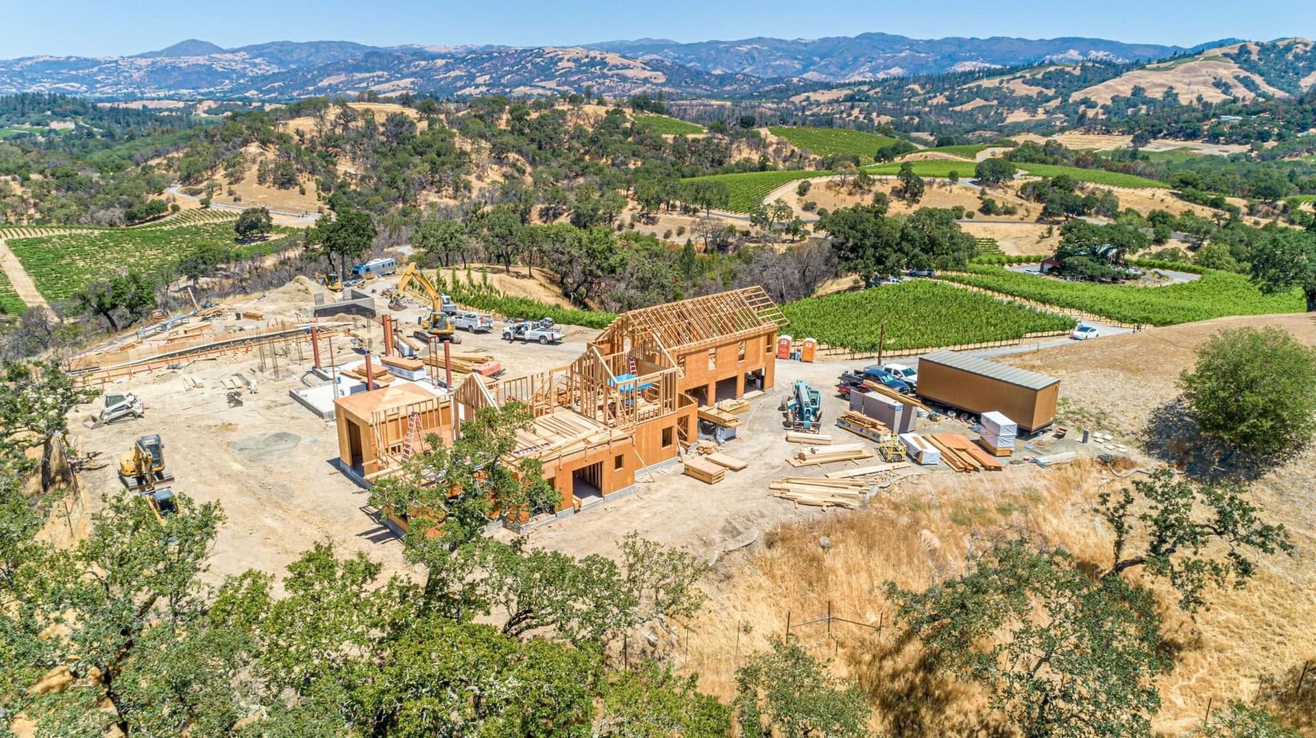 Aerial view of a house under construction on a hillside with trees and rolling hills in the background