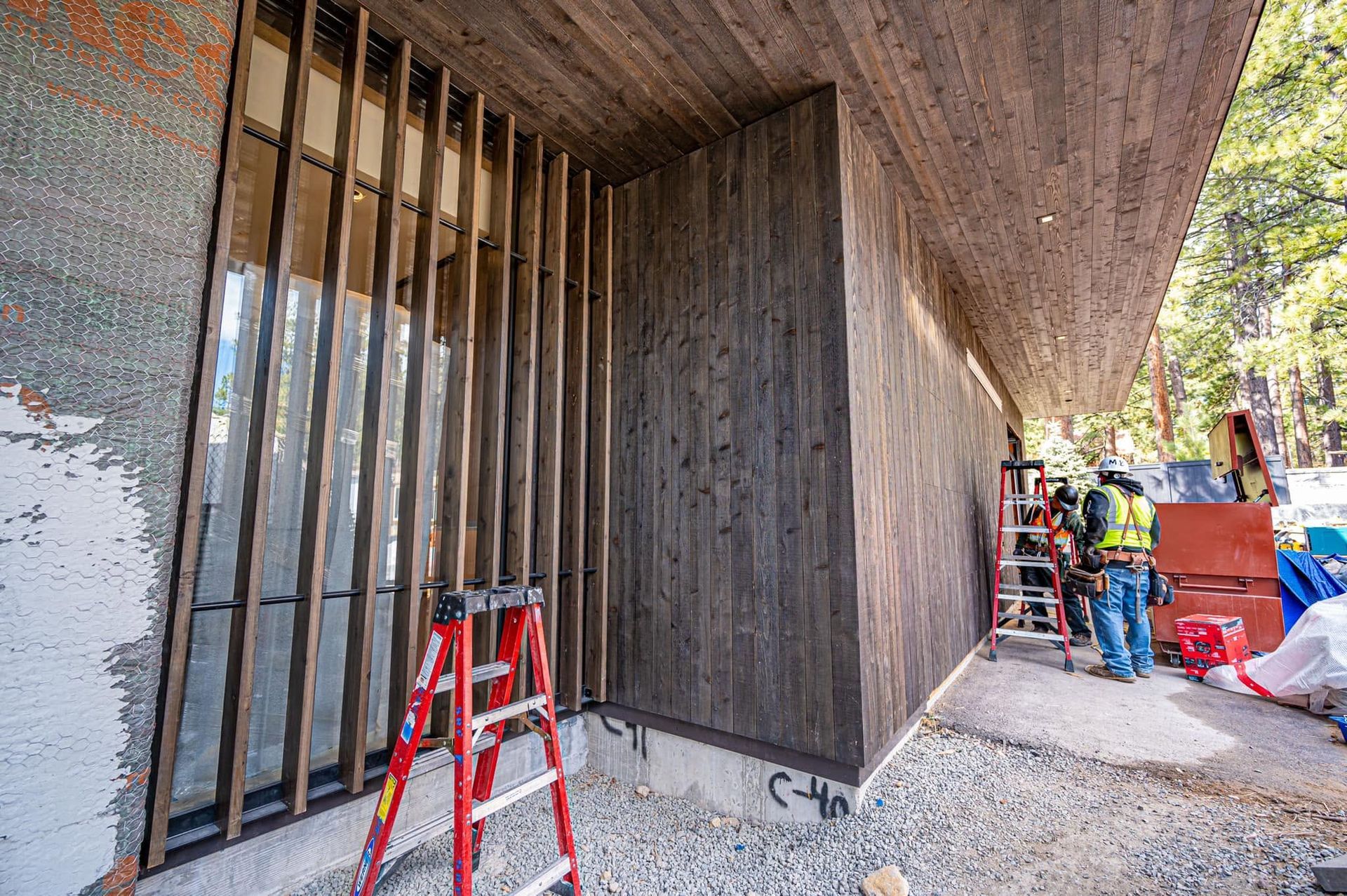 Construction workers near a concrete wall and barred opening, with a red ladder and tools on site