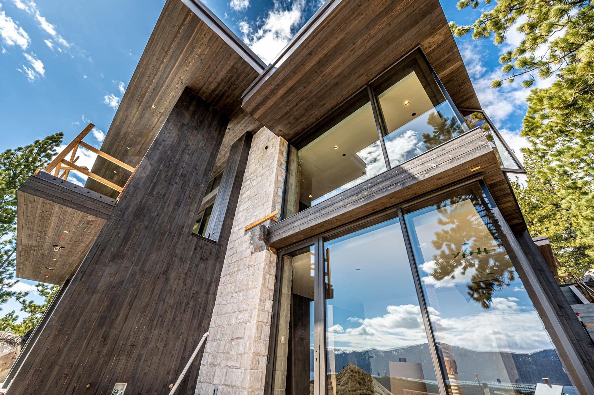 Modern home exterior with wood siding, stone wall, and large glass windows under a blue sky