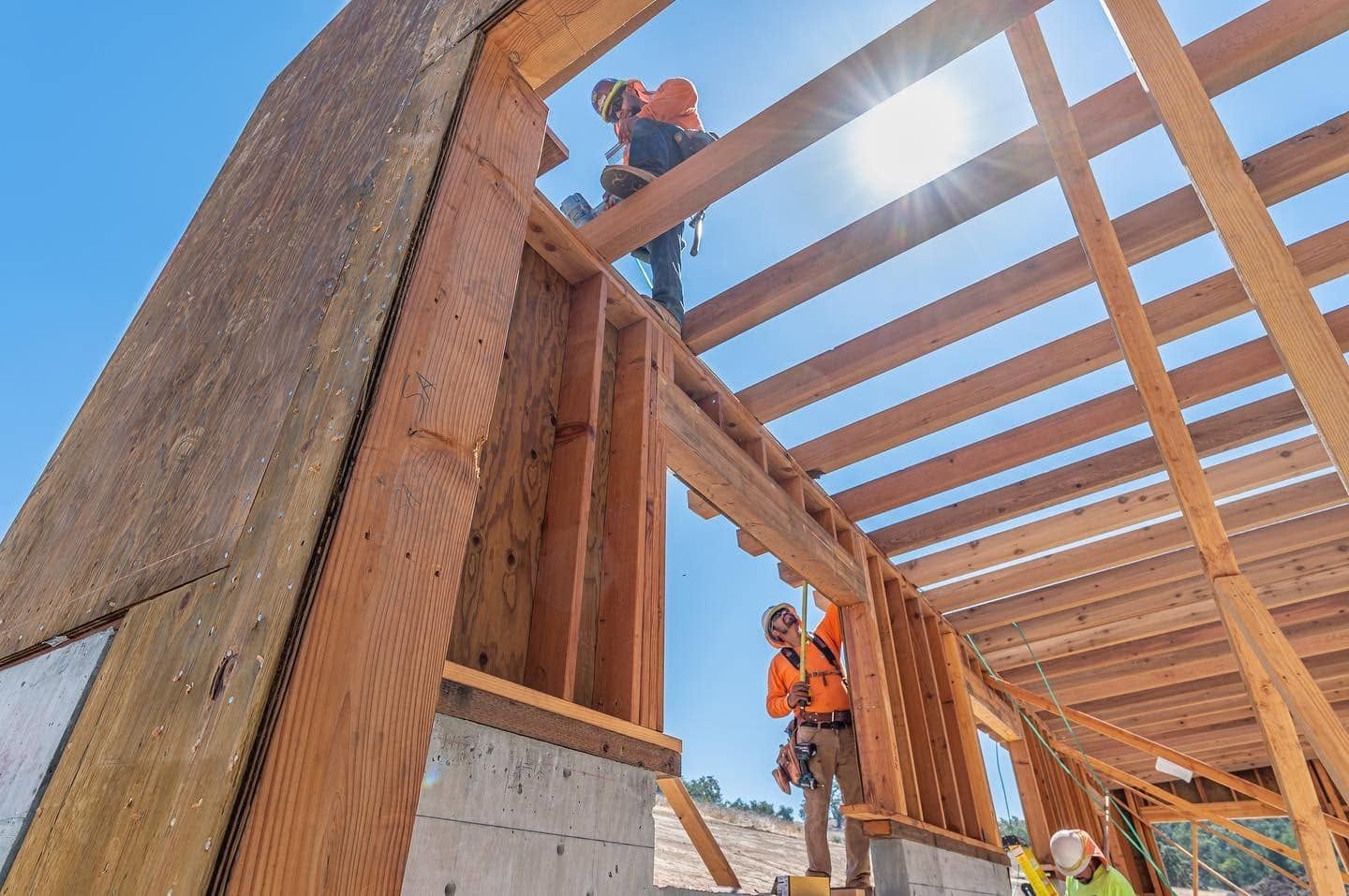 Construction workers framing a wooden building structure under a bright blue sky