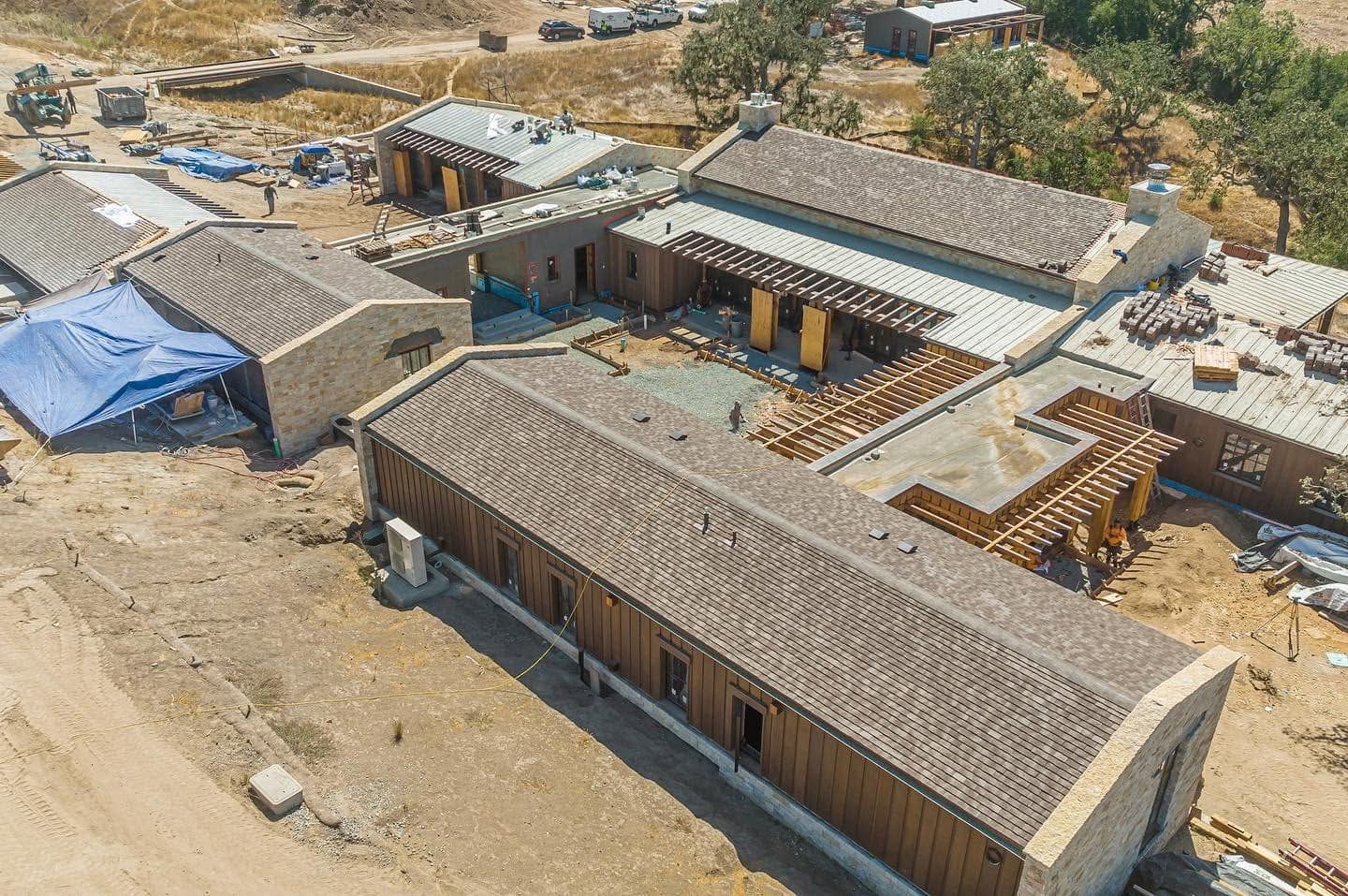 Aerial view of a rural building complex with tiled roofs, dirt yard, and a blue tarp shelter.
