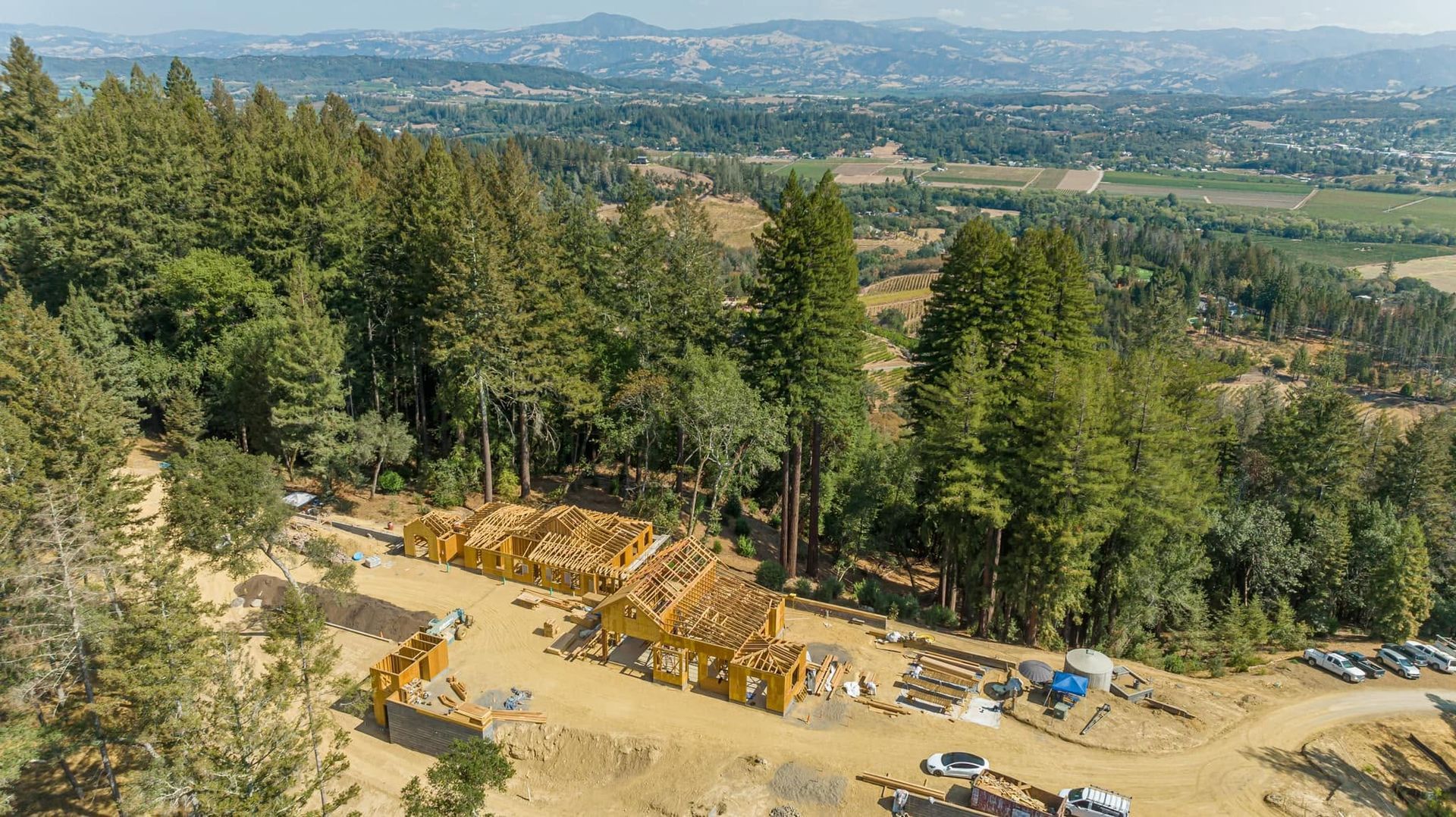 Aerial view of a forested hillside construction site overlooking a wide valley and distant mountains