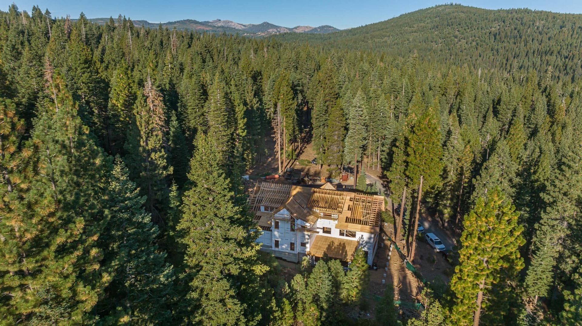 Aerial view of a house surrounded by dense evergreen forest and distant hills