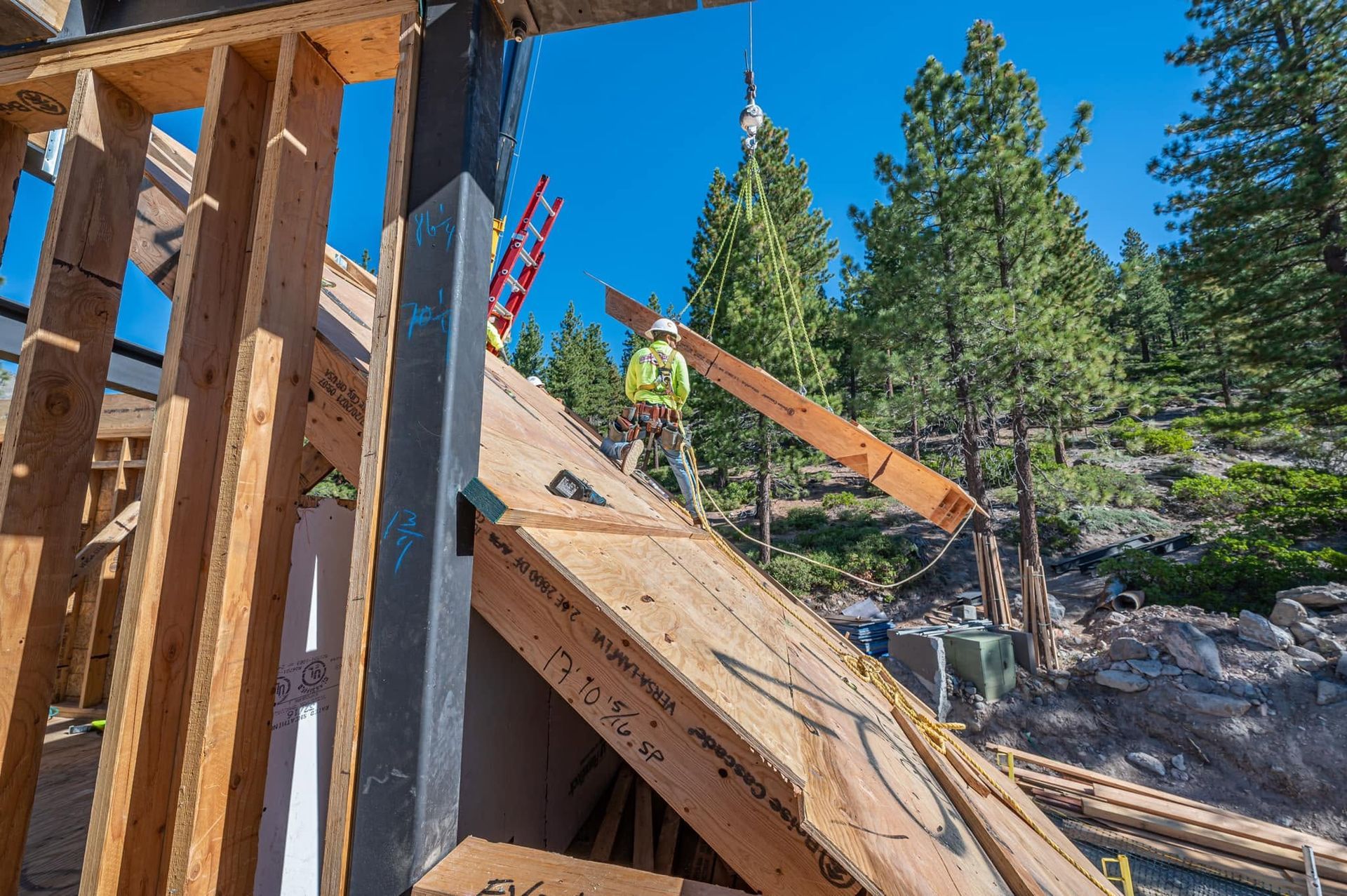 Construction site with wooden framing, sloped lumber, and workers on a rocky hillside under blue sky