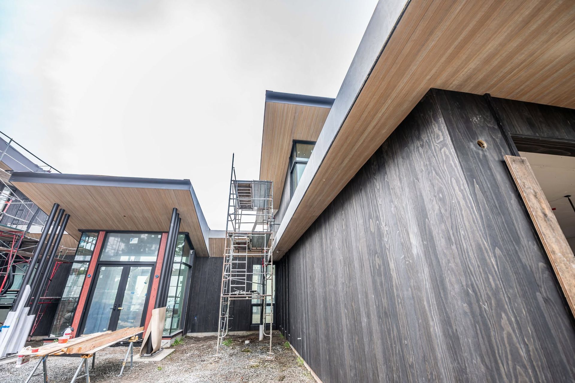 Modern building exterior with scaffolding and construction materials between wood-paneled walls