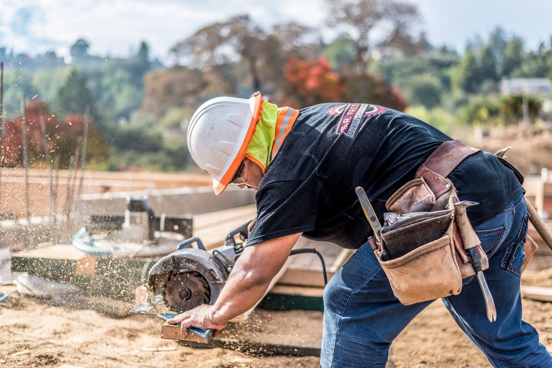 Construction worker cutting concrete with a circular saw outdoors, wearing a hard hat and safety vest.