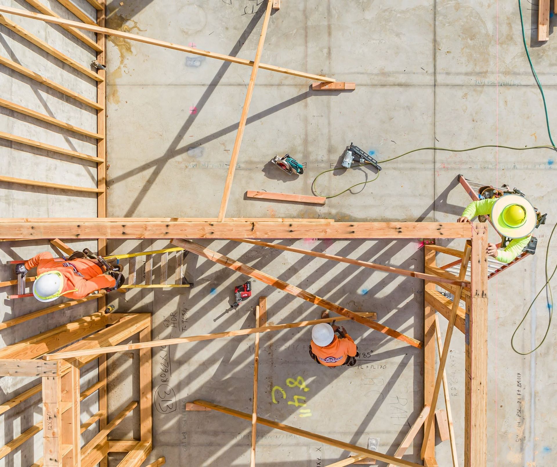 Construction workers on a wooden frame deck, viewed from above, with tools and safety helmets.
