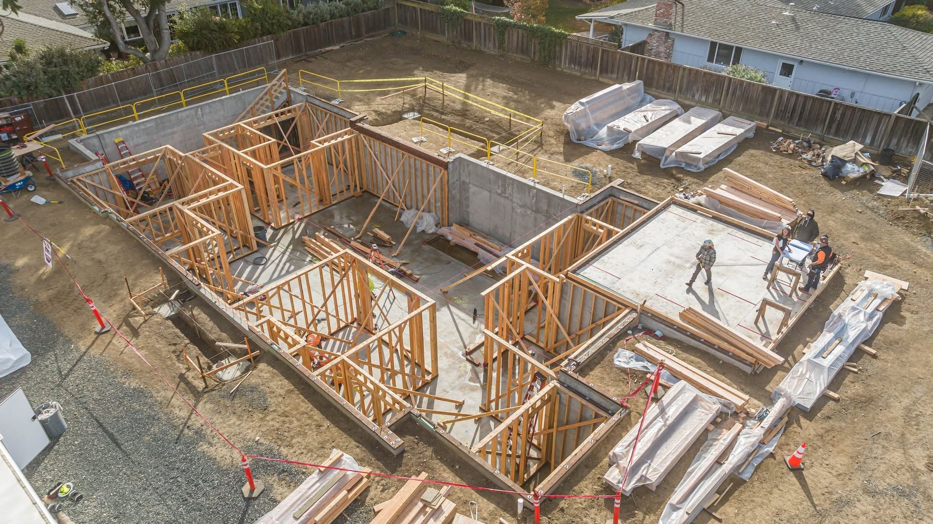 Construction site with wooden house framing and a concrete foundation, viewed from above.