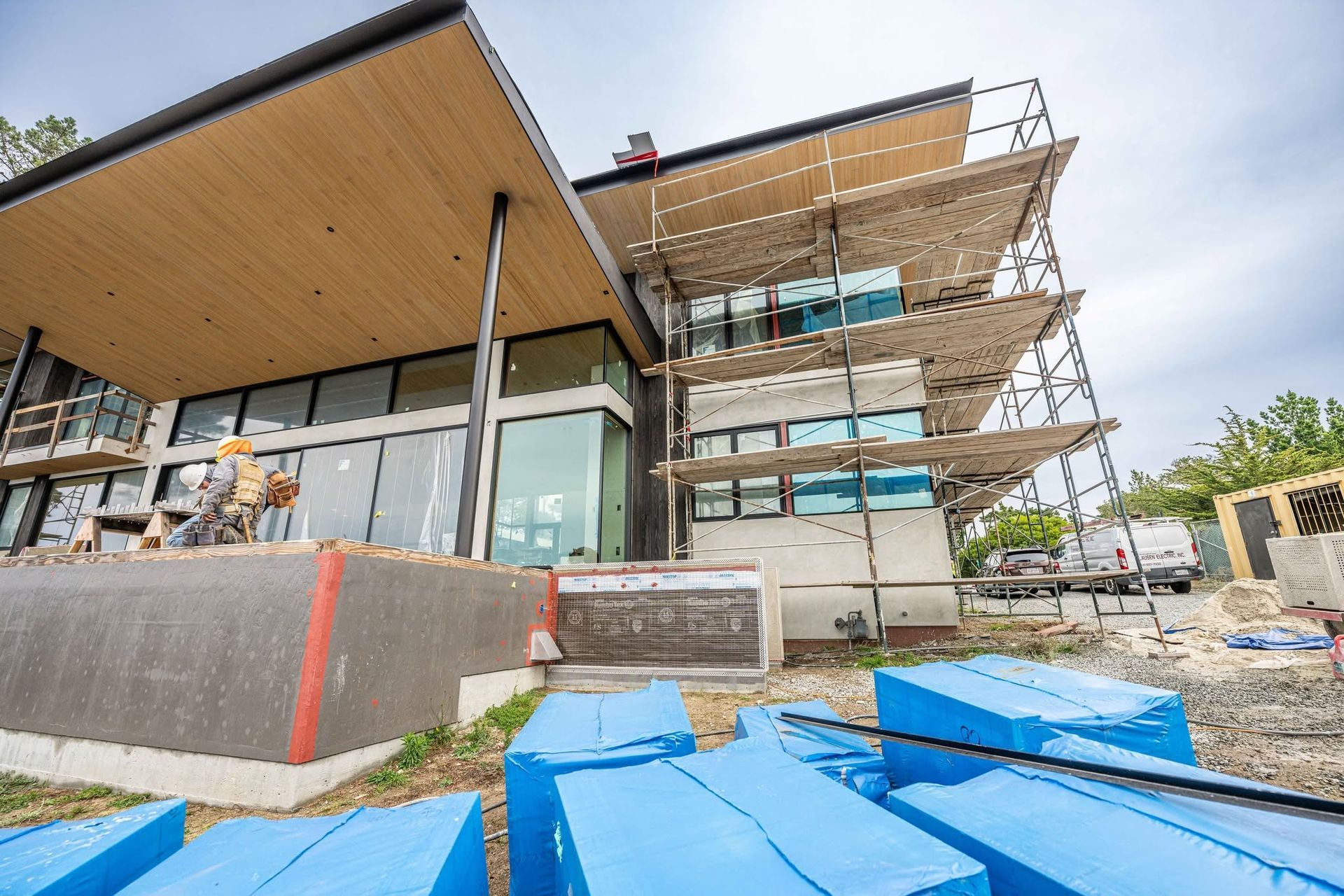 Modern house under construction with scaffolding, blue tarps, and exposed framing