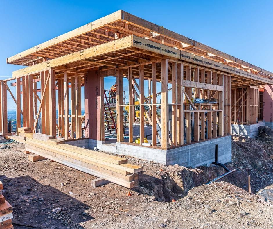 Wood-framed house under construction with exposed beams and siding on a dirt lot.