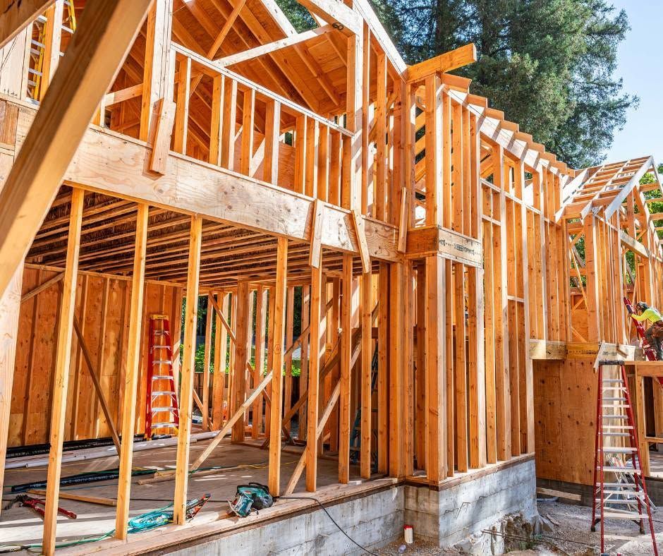Wood-framed house under construction with exposed beams and a ladder on the right side