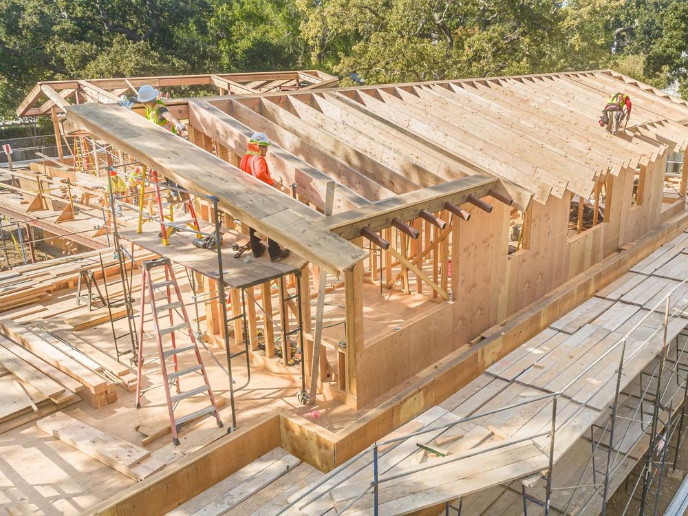 Wooden house under construction with scaffolding and workers on a partially framed roof