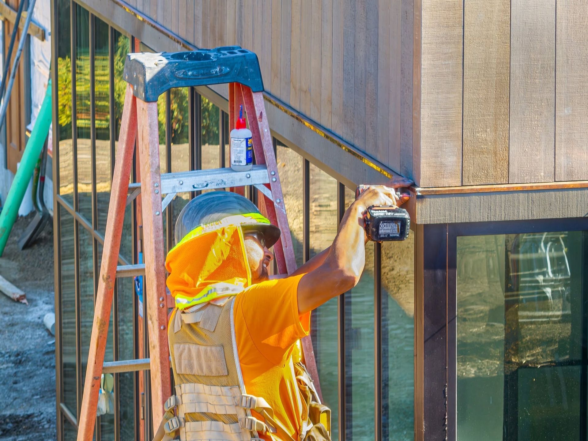 Worker on ladder inspecting exterior wall siding with a handheld device