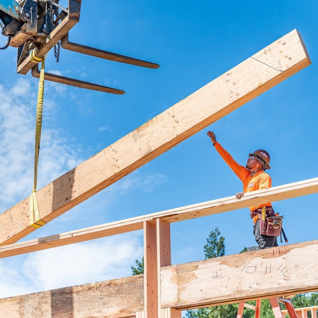 Construction workers lifting a wooden beam at a building site under a blue sky