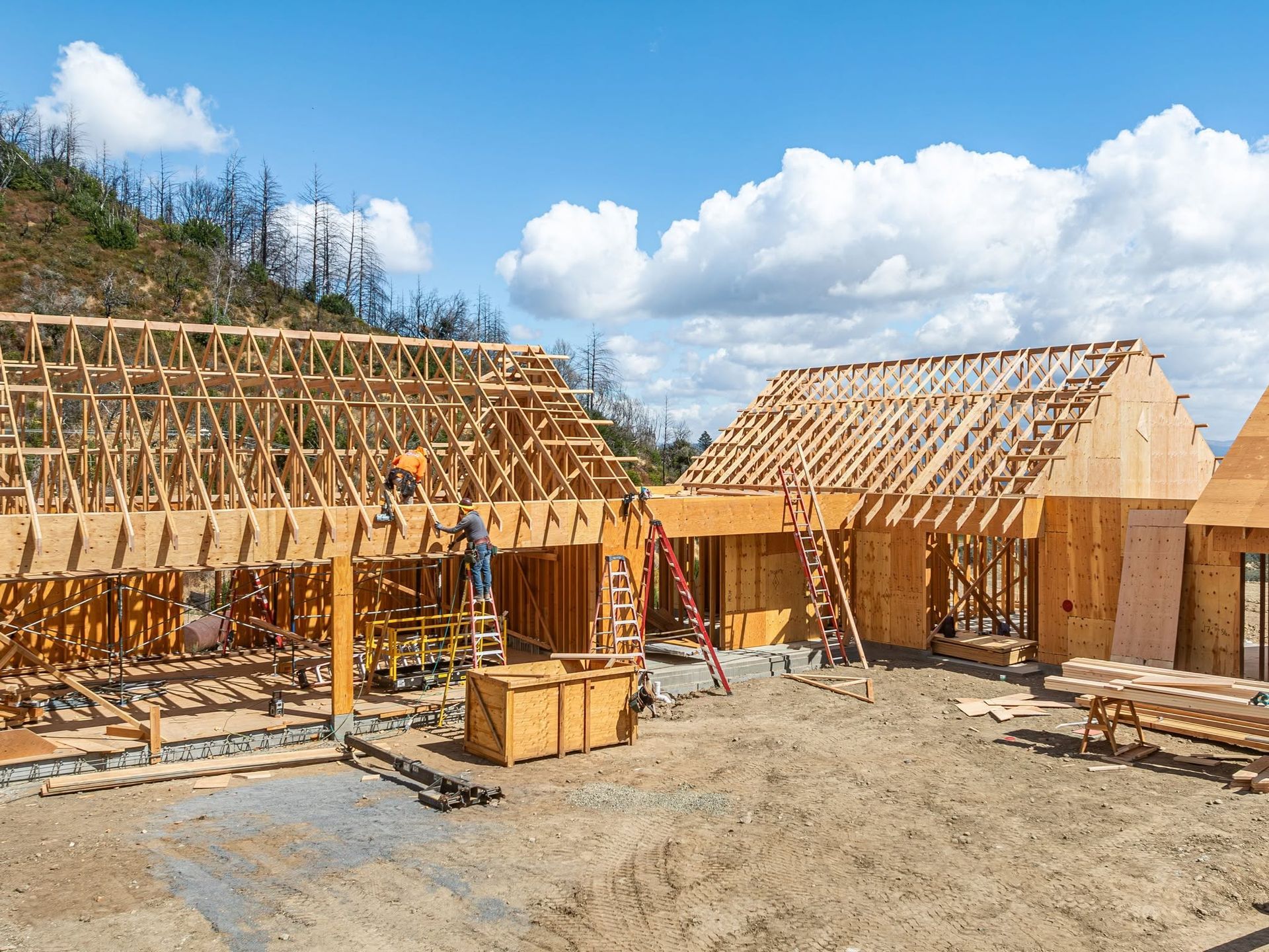 Wood-framed houses under construction on a sunny site with blue sky and clouds
