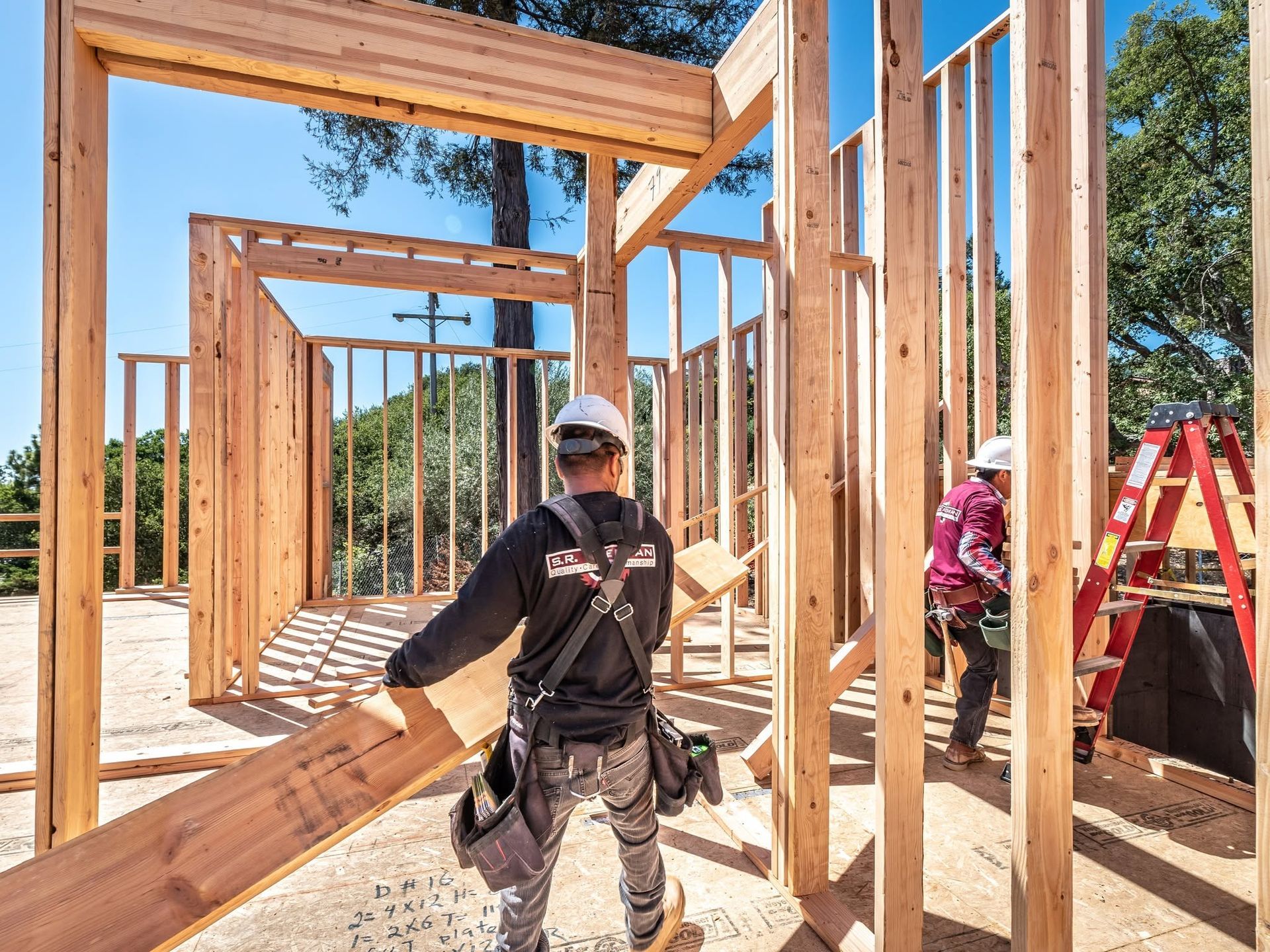 Construction workers framing a wooden house structure in bright daylight.