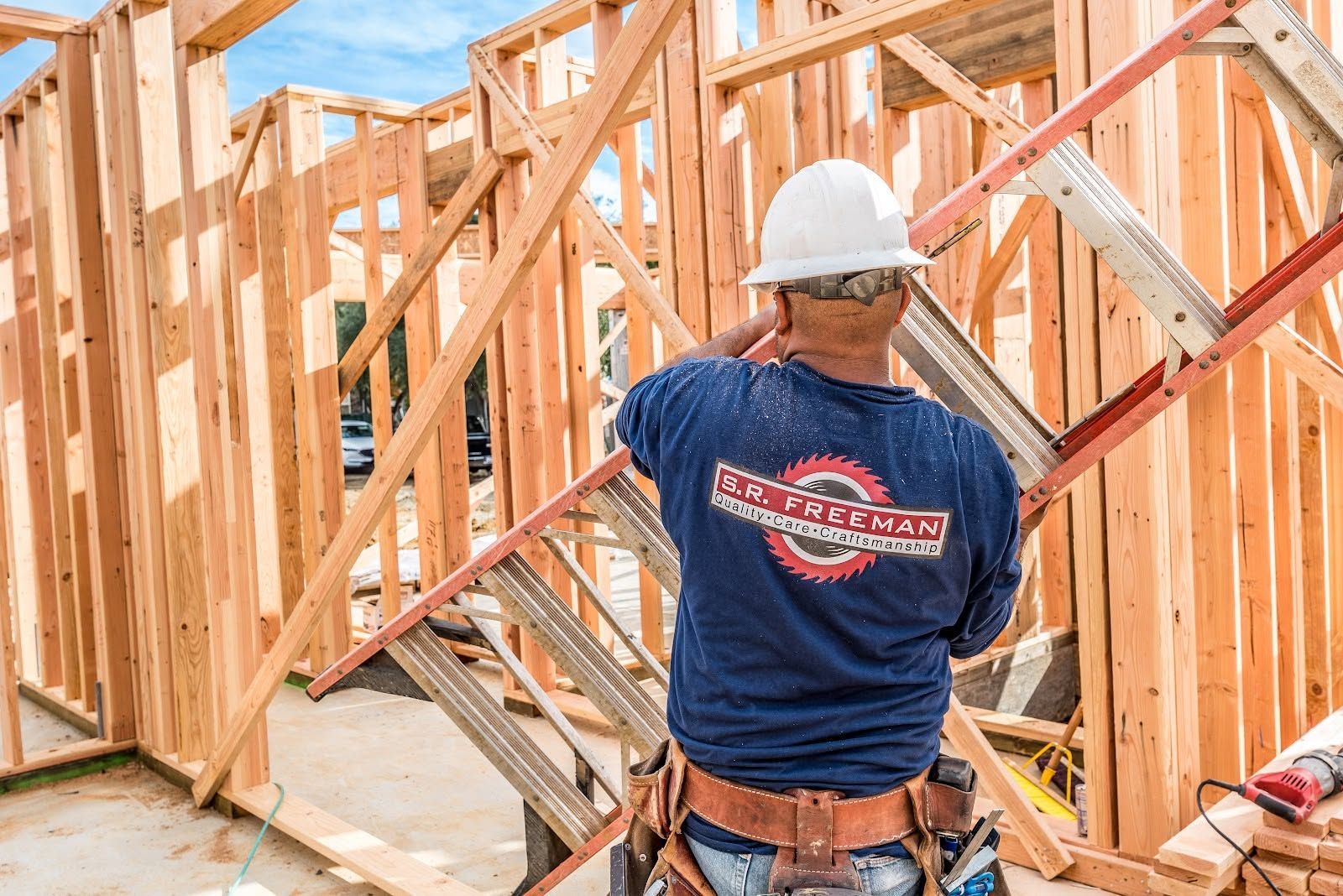Construction worker in hard hat framing a wooden house structure at a building site