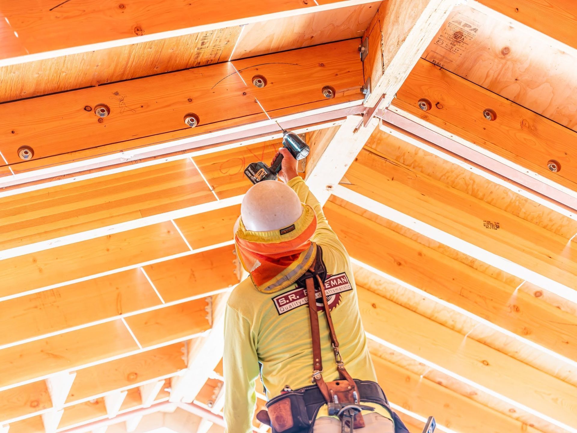 Construction worker installing insulation in an orange wooden attic ceiling