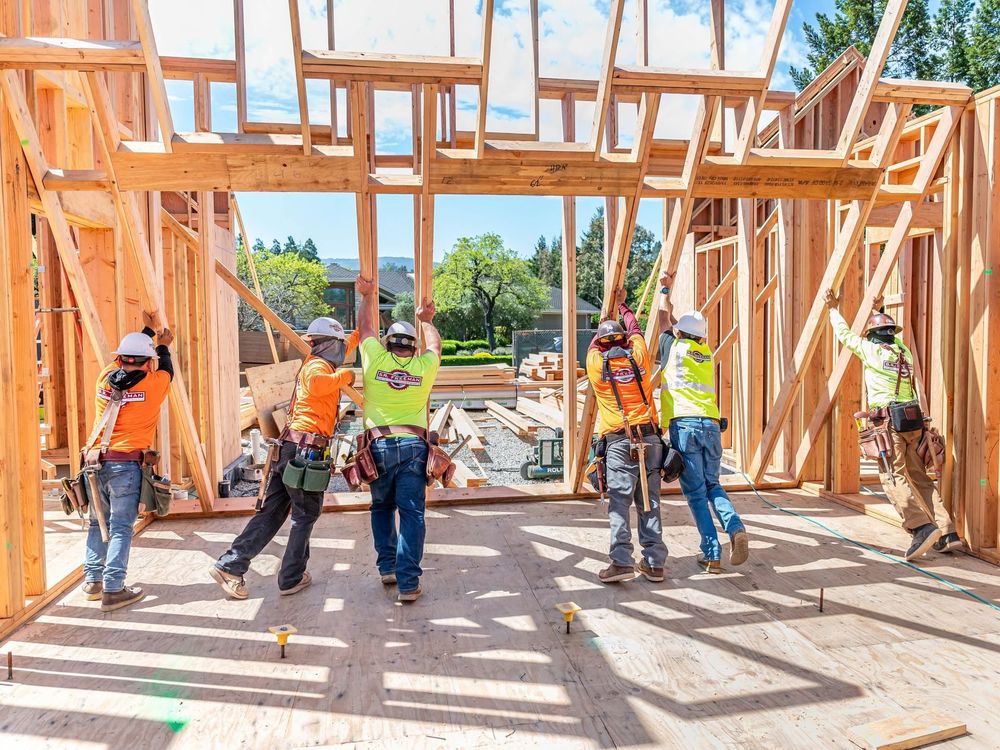 Construction workers framing a wooden house skeleton at a sunny building site