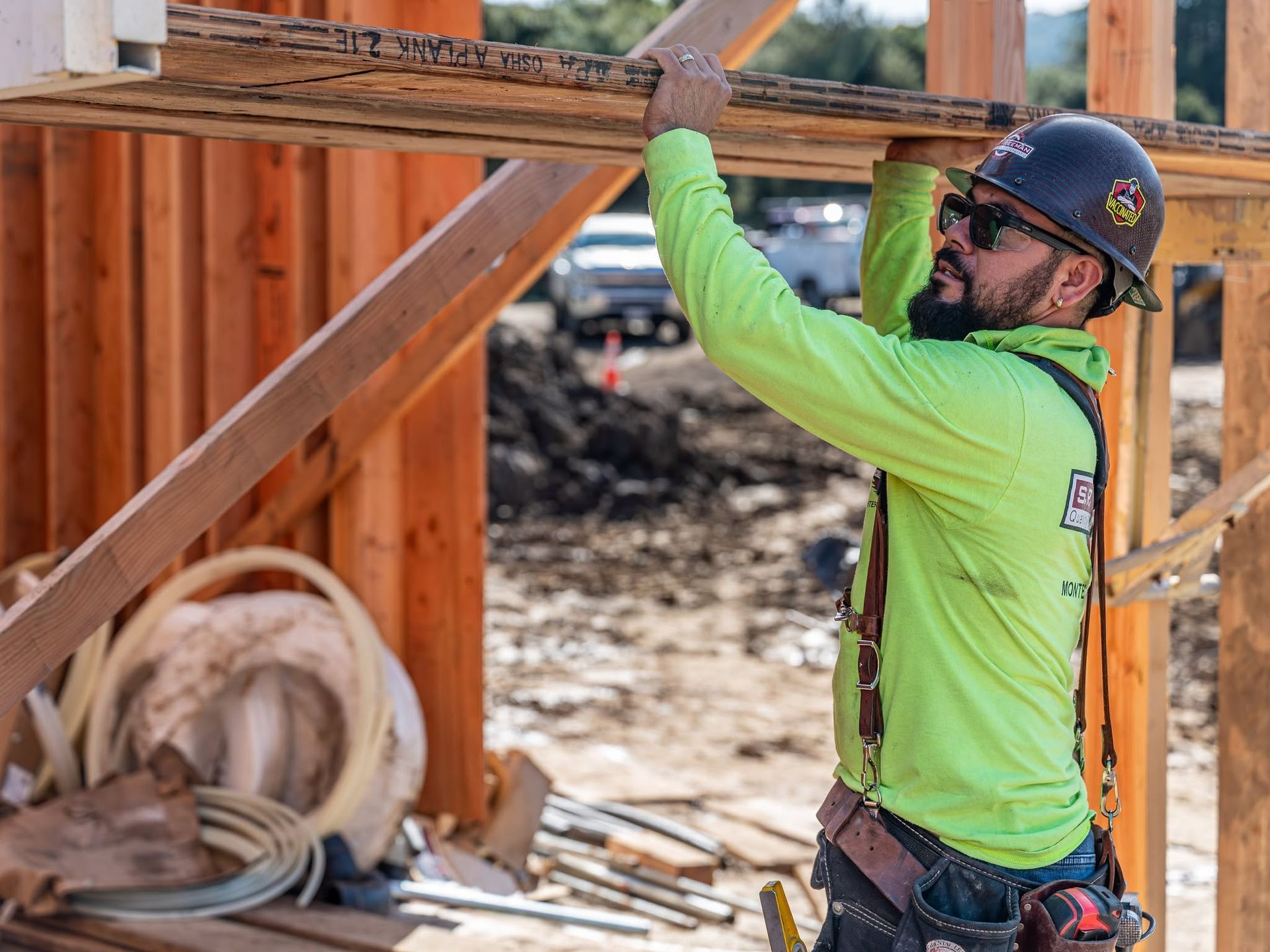 Construction worker in neon green shirt and hard hat fastening a wooden beam at a building site