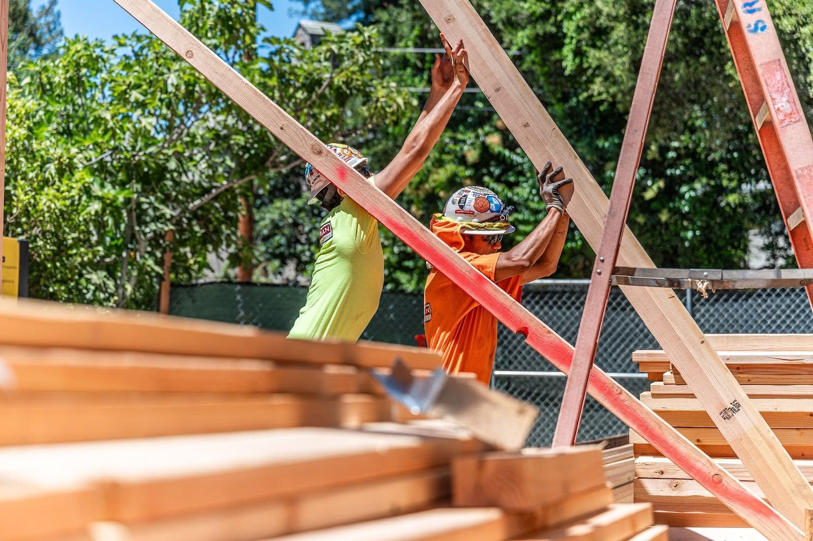 Workers in bright vests and hard hats among wooden beams at a construction site outdoors