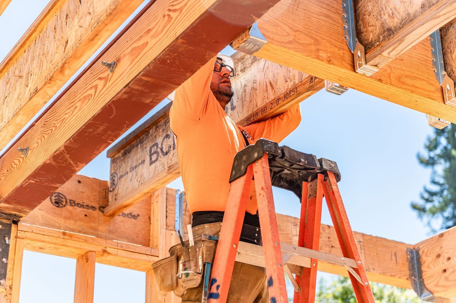 Worker on a ladder installing wooden framing on a house under construction