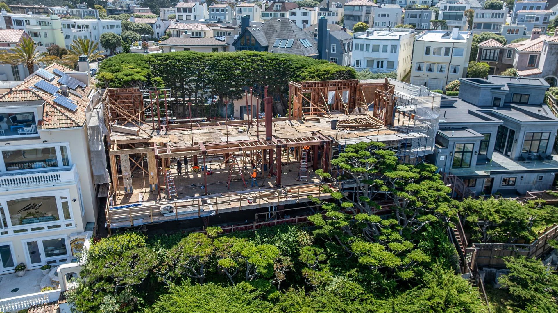 Burned-out building shell amid dense white city rooftops and green trees, seen from above