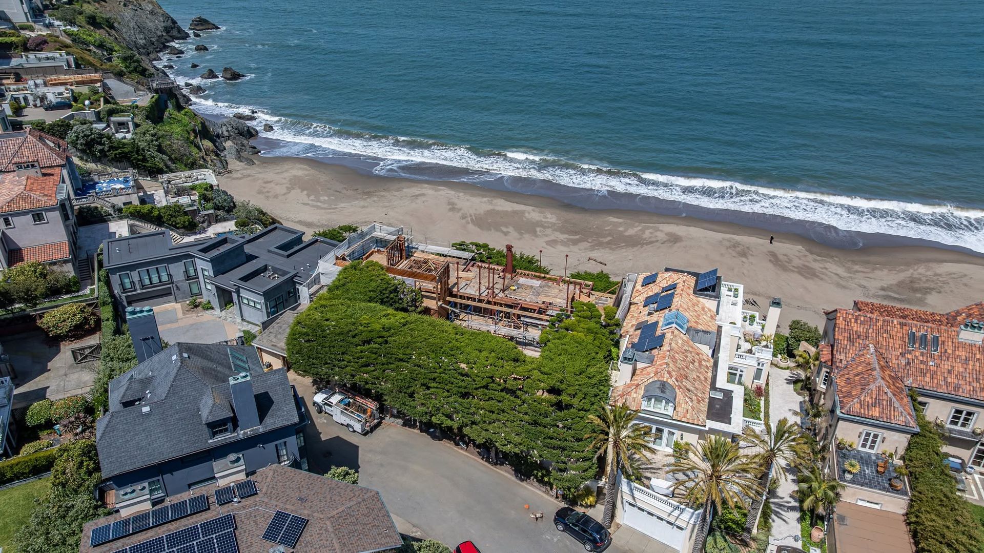 Aerial view of beachfront homes, sandy shore, and blue ocean waves on a sunny day