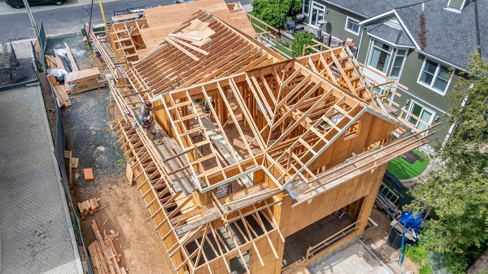 House under construction with exposed wooden roof framing beside neighboring homes