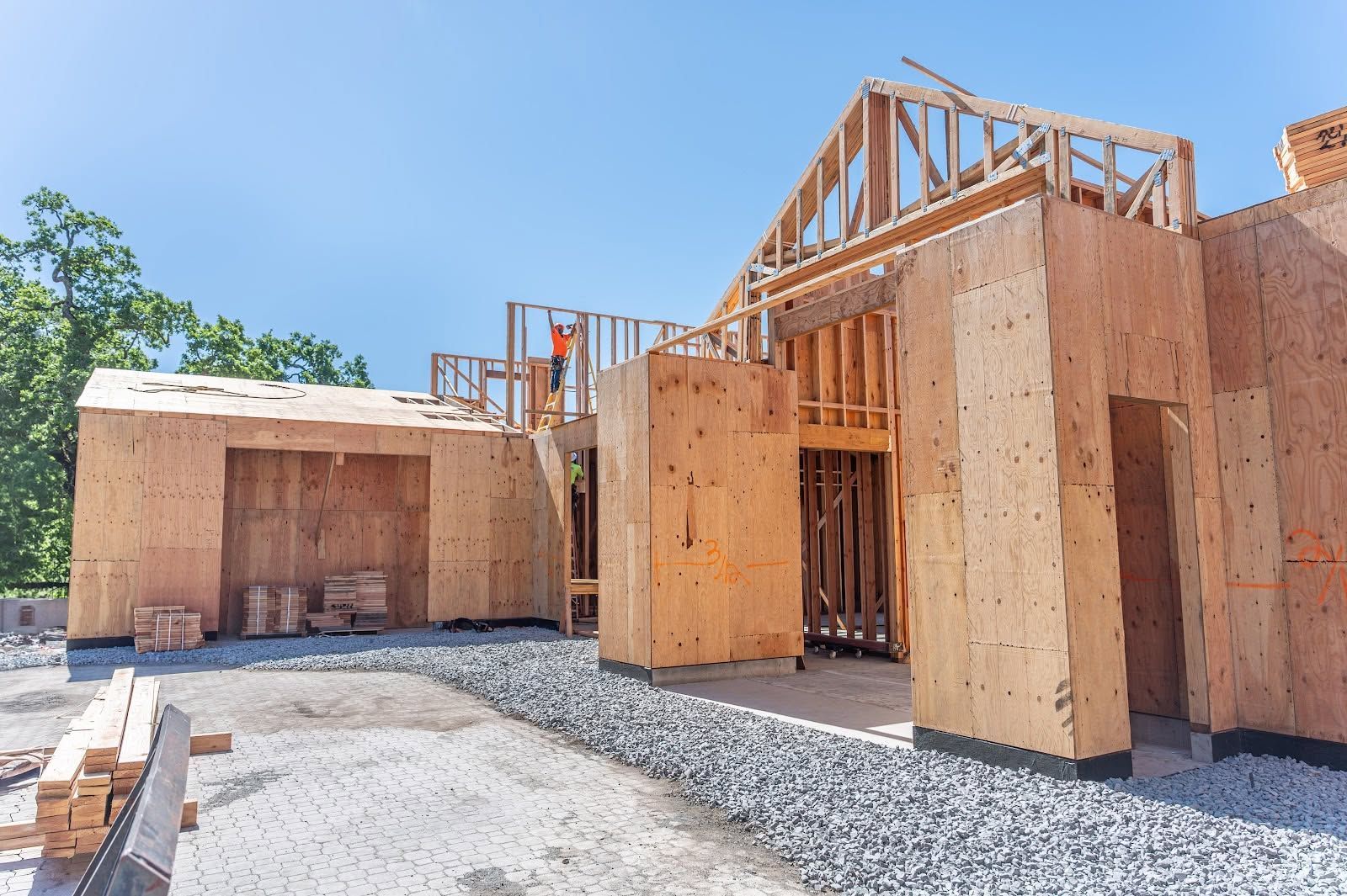 Partially built wooden house framing on a gravel lot under a clear blue sky