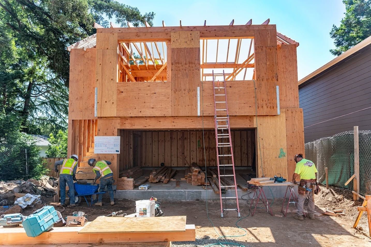 Partially built two-story wooden house under construction, with ladders and workers at the front.
