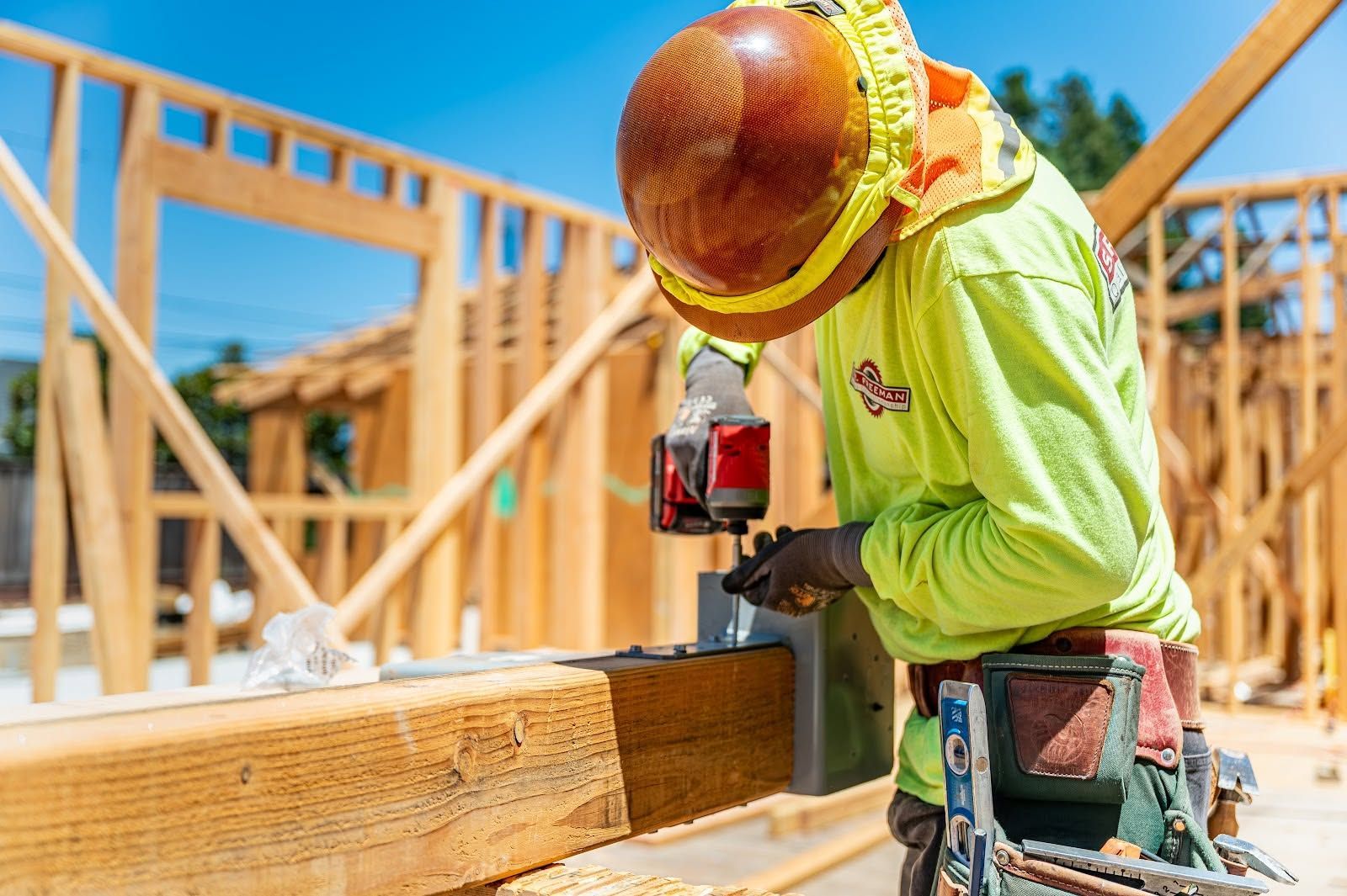 Construction worker using a nail gun on a wooden frame at a sunny building site