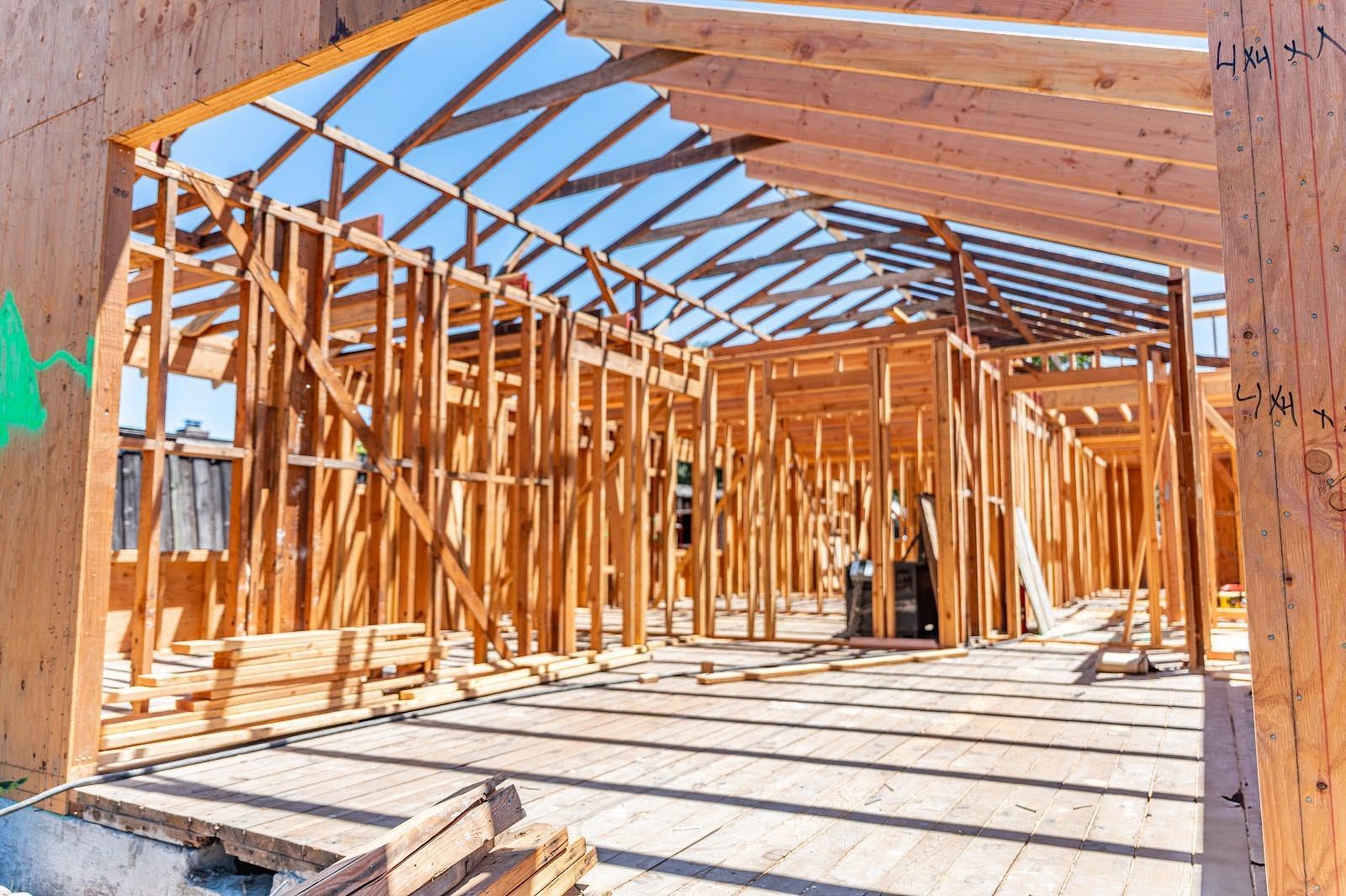 Wood-framed house under construction with exposed beams and bright sunlight streaming through the open structure