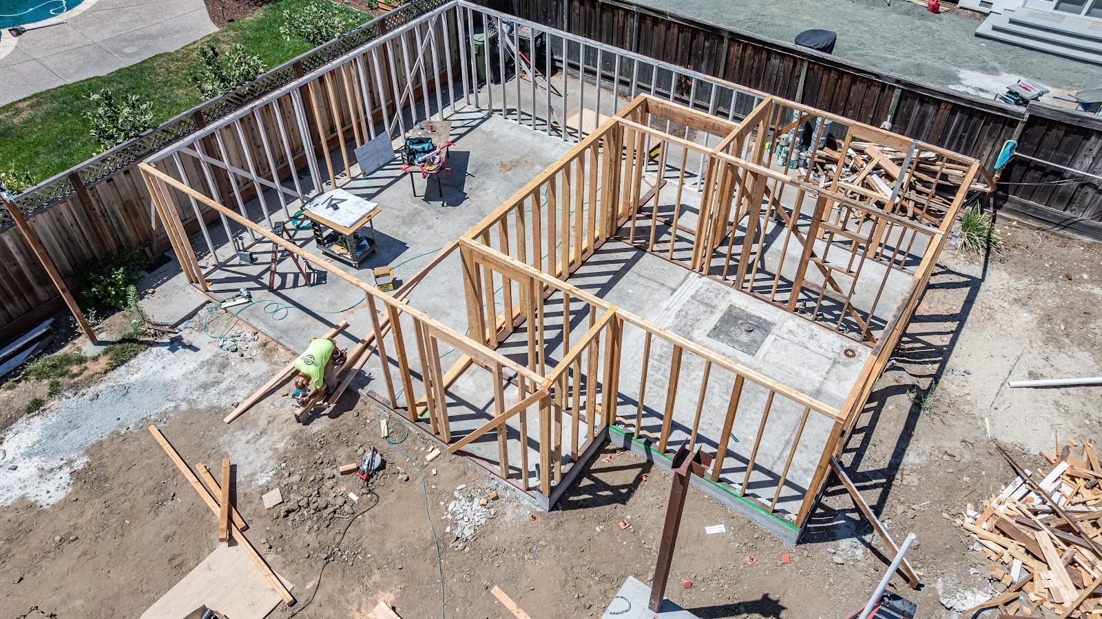 Aerial view of a house foundation under construction with wooden framing, concrete slab, and building materials.