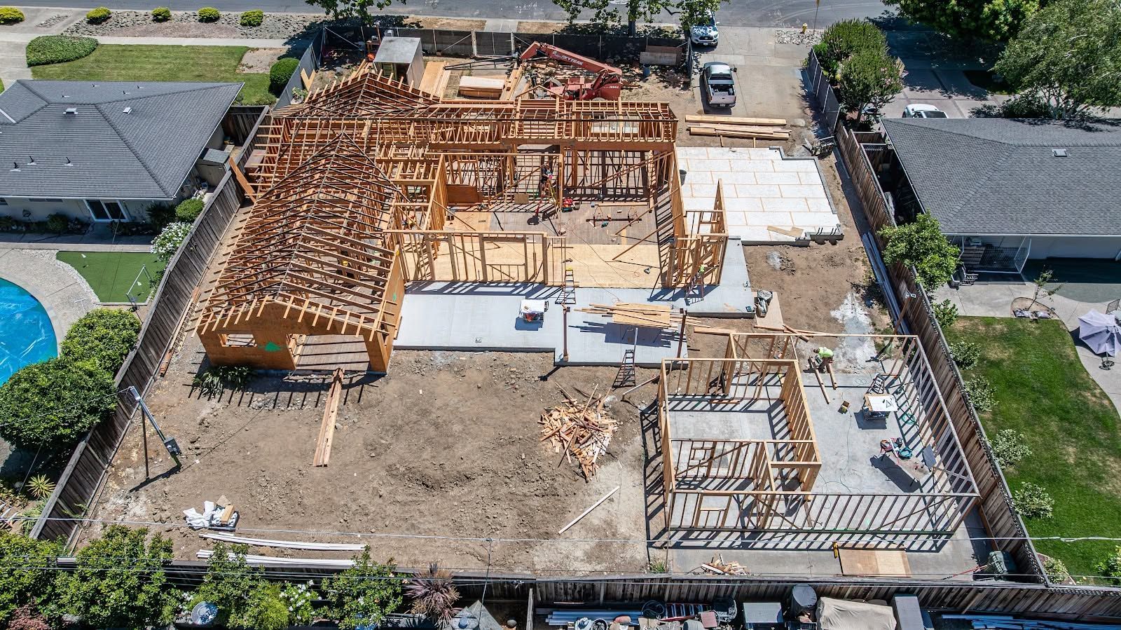 Aerial view of a house foundation under construction with wooden framing and concrete slabs on a lot
